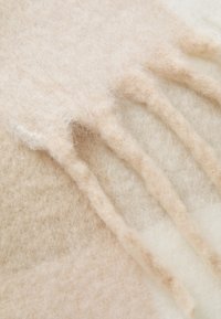 Uld tørklæde i en blanding af beige og creme nuancer, med frynsede kanter og en blød, fuzzy tekstur.