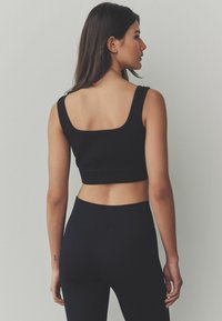 Black ribbed crop top with wide straps and square neckline, paired with matching high-waisted leggings. Smooth texture, form-fitting design.