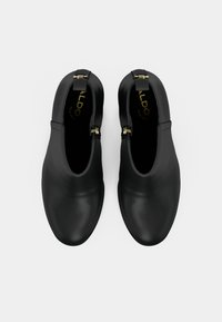 Bottes de cheville en cuir noir avec une texture lisse, accents de boucle dorée, pointes arrondies et design minimaliste. Intérieur doublé avec logo.