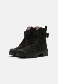 Botas negras con un diseño robusto, suela de goma, parte delantera con cordones y correa ajustable. Fabricadas en un tejido texturizado con acabado mate.
