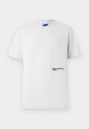 Camiseta de algodón blanca con cuello redondo y mangas cortas. Presenta un logo impreso "KARL LAGERFELD JEANS" en negro en el lado izquierdo.