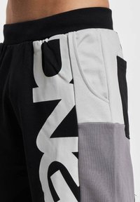Black and gray sweatpants feature a white logo, side pocket on the left, and a mix of fabric textures across different areas.