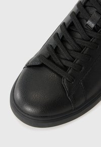 Black leather sneaker featuring a rounded toe, textured finish, flat laces, and a contrasting rubber sole. Simple, minimal design with seamless accents.