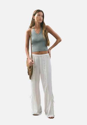 Top corto de canalé gris claro combinado con pantalones palazzo blancos con detalles de encaje. Los accesorios incluyen un bolso cruzado marrón con flecos.