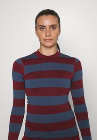 Langermet topp med horisontale striper i burgunder og blått. Slim fit med høy hals og glatt, elastisk materiale.