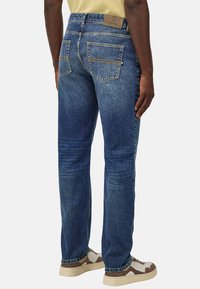 Temno modri jeans z ravnim krojem, ki vsebujejo dva zadnja žepa, kontrastno šivano in označeno usnjeno nalepko na pasu.
