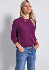 Lila stickad tröja med rund halsringning, ribbade muddar och en avslappnad passform, som är kombinerad med ljusblå denimjeans. Mjuk textur och avslappnad stil.
