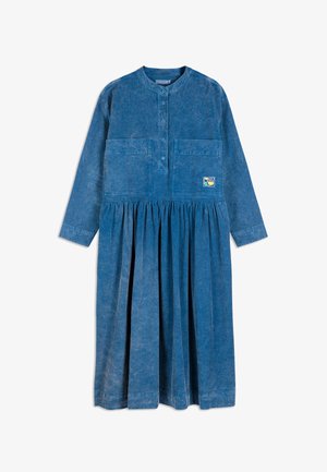 Abito in corduroy blu a maniche lunghe con gonna arricciata, chiusura anteriore con bottoni, due tasche sul petto e una piccola patch colorata sulla tasca destra.