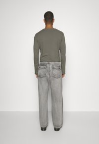 Pitkähihaista oliivinvihreää paitaa on paritettu löysästi istuvien vaaleanharmaiden farkkujen kanssa, joissa on kaksi takataskua ja näkyvät ompeluyksityiskohdat.