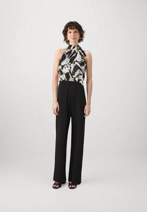 Combinaison noire avec un col halter, présentant un corsage à motifs floraux en noir, blanc et jaune. Le tissu a une texture lisse.