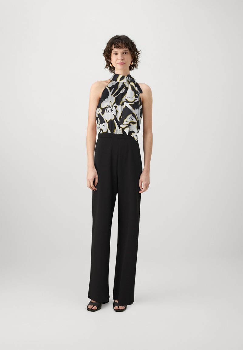 Svart jumpsuit med halterneck, med et blomstermønstrete liv i svart, hvitt og gult. Stoffet har en glatt tekstur.