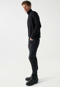 Črni pulover z rolko, prilega se; v kombinaciji z temnimi kavbojkami in debelimi črnimi gležnjarji. Preproste, gladke teksture in čiste linije.