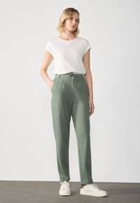 Lys grønne joggebukser med snor i livet, sidelommer og en glatt tekstur, kombinert med en hvit t-skjorte med korte ermer og joggesko.