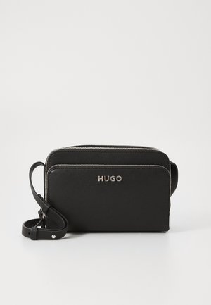 Czarna skórzana torba na ramię z srebrnymi zamkami, regulowanym paskiem i logo "HUGO" na przedniej kieszeni.