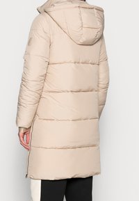 Chaqueta acolchada beige con capucha, diseño acolchado y cremalleras laterales. Presenta un tejido suave y brillante y un corte de longitud media, adecuada para el clima frío.