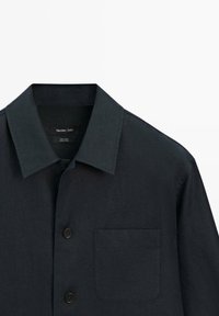 Chemise en lin bleu marine foncé avec col classique, poche avant à gauche et deux boutons noirs visibles à l'avant.