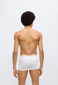 Λευκά βαμβακερά μποξεράκια με ελαστική μέση που φέρει το λογότυπο "Tommy Hilfiger" σε μαύρο και κόκκινο. Η εφαρμογή είναι στενή και προσαρμοσμένη στο σώμα.