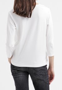 Haut blanc léger à manches longues avec un col rond et un ourlet arrondi. Associé à un jean gris foncé avec des poches arrière et des coutures discrètes.