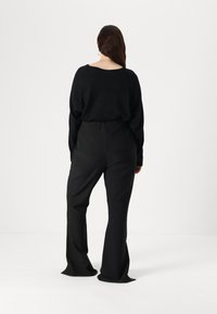 Pulover negru supradimensionat și pantaloni largi, fabricați dintr-un material moale. Puloverul are o gât de spate adânc; pantalonii au o croială netedă și ajustată.