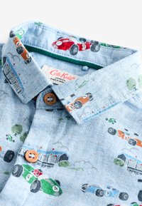 Camicia azzurro chiaro con motivo a spina di pesce decorata con automobili colorate ricamate. Chiusura con bottoni marroni e dettaglio verde all'interno del colletto.