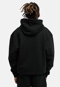 Black oversized hoodie with a large hood, made of soft fabric. Features a simple design and loose fit, with ribbed cuffs and hem.