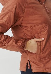 Veste matelassée couleur rouille avec une fermeture éclair sur le devant, des poignets élastiques et une poche sur le côté. Tissu lisse avec une finition légèrement brillante.