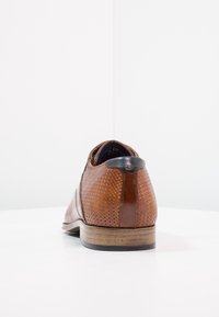 Chaussure en cuir marron avec texture tissée, bout arrondi et accent de talon noir. Présente une semelle marron clair et une doublure intérieure lisse.