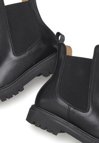 Zwarte leren enkelboots met elastische zijpanelen, gestructureerde rubberen zolen en een trekhaak, ontworpen voor gemakkelijke draagt en comfort.