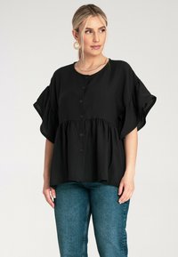 Czarna bluzka peplum z krótkimi, szerokimi rękawami, z przodu zapinana na guziki, wykonana z teksturowanej tkaniny. Połączona z niebieskimi dżinsami o wysokim stanie.