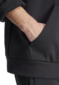 Zwarte sweatshirt met een kangoeroezak en ribgebreide manchetten, met een gladde textuur en een aansluitende tailleband.