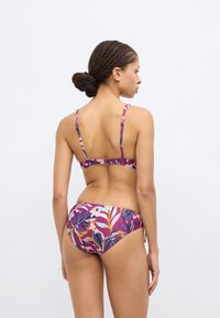 Σετ μπικίνι με λουλουδάτο, πολύχρωμο τροπικό μοτίβο. Το πάνω μέρος έχει λεπτές τιράντες και κλείνει με κούμπωμα στην πλάτη. Το κάτω μέρος είναι μεσαίας μέσης με ίδια σχεδίαση.
