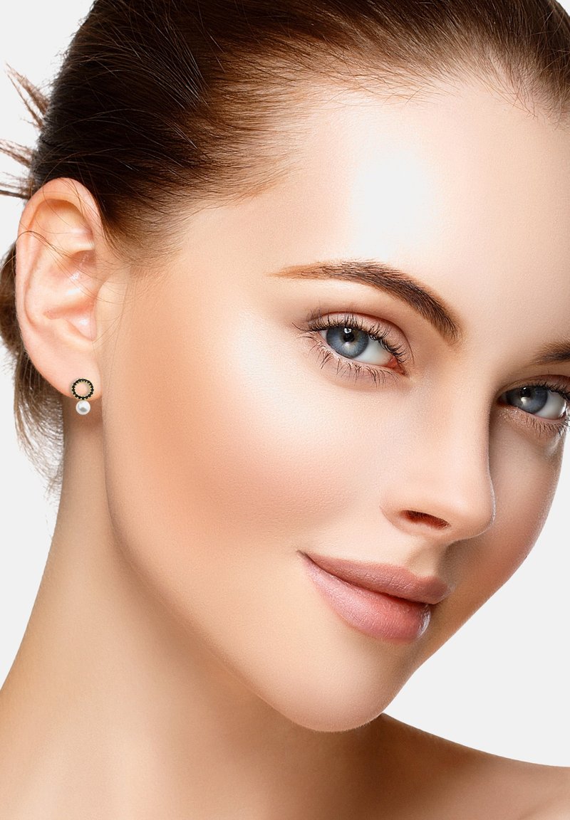 Guldtonade cirkulära örhängen har en svart emaljaccent och ett vitt pärlhänge. Modellen bär örhängena med slätt, bakåtkammat hår mot en neutral bakgrund.
