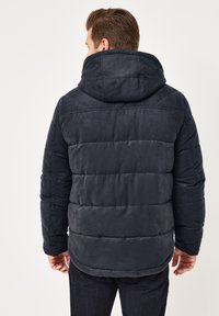 Dunkelblaue Daunenjacke mit plüschiger Textur, horizontaler Steppung, einer großen Kapuze und elastischen Bündchen.