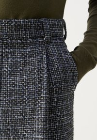 Pantaloni navy tricotati cu un model texturat, având un talie ajustată și buzunare laterale. Materialul include fire albe și albastre deschise.