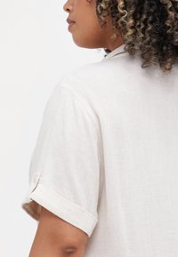 Light beige short-sleeve shirt made of textured fabric, featuring a roll-up sleeve with a button detail and a simple collar design.