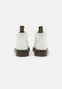 Botas de tobillo de piel blanca con lengüetas de tirón negras y amarillas, suelas estriadas marrones y costuras naranjas a lo largo del borde de la suela.