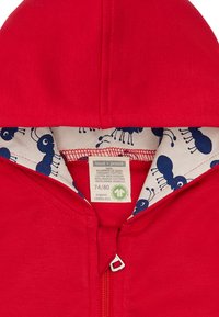 Felpa rossa con cappuccio e zip, con interno crema e fantasia di formiche blu. Realizzata in 100% cotone biologico. Taglia 74/80.