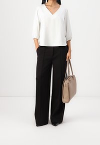 Blouse blanche à col en V avec manches trois-quarts, associée à un pantalon noir taille haute à jambes larges. Sac à main beige avec deux poignées.