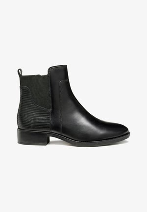 Bottine en cuir noir avec un panneau élastique texturé noir, bout rond et un petit talon bloc. Surface lisse avec un éclat subtil.