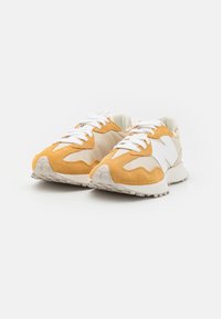 Un paio di sneaker in suede beige e arancione con lacci bianchi e suole spesse su uno sfondo bianco.