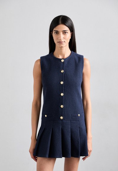 Robe sans manches bleu marine en tissu texturé, avec un col rond, des boutons dorés et un design de jupe plissée. Poches avant incluses.