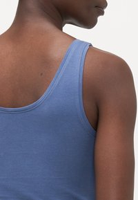 Blå tanktop laget av bomull, med en glatt tekstur, rund halslinning og tynne stropper. Synlig søm langs kantene.