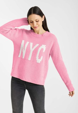 Roze gebreide trui met een ronde hals en lange mouwen, voorzien van een grote witte "NYC" grafiek over de voorkant. Zachte textuur en geribbelde zoom.