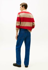 Sweter w paski w kolorze czerwonym i beżowym, zestawiony z niebieskimi dżinsami. Sweter ma luźny fason i ściągacze u rękawów. Całość dopełniają czarne buty.