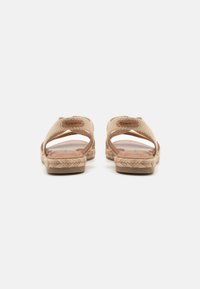 Beige sandals featuring cross-strap design, woven textile upper, and braided jute midsole. Flat, anti-slip sole. Brand logo visible.