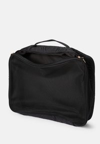 Sac en tissu matelassé noir avec une façade en maille, fermetures éclair dorées, double poignée de transport et un intérieur spacieux pour le rangement. Conçu pour l'organisation.