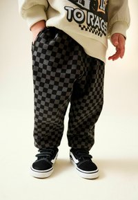 Pantaloni în carouri negre și gri, realizați dintr-un material moale, cu talie elastică și buzunare laterale, asortați cu adidași negri.