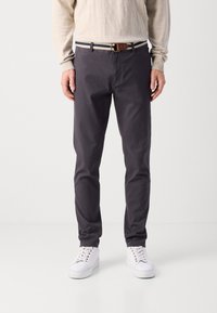 Dunkelgraue Baumwoll-Chinos für Herren mit schlanker Passform, ausgestattet mit einem Taillenbund und einem blau-weiß gestreiften Gürtel sowie weißen Sneakers.
