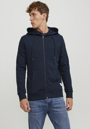 Navy zip-up hoodie in soft fabric with a drawstring hood, front pocket, and ribbed cuffs. Notable for its minimal design and sleek finish.