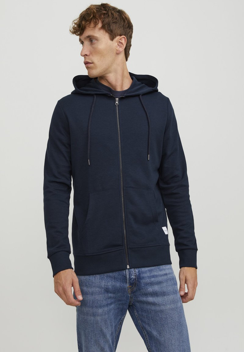 Marineblå zip-up hoodie i blødt materiale med snorhætte, frontlomme og ribbede manchetter. Kendt for sit minimale design og elegante finish.